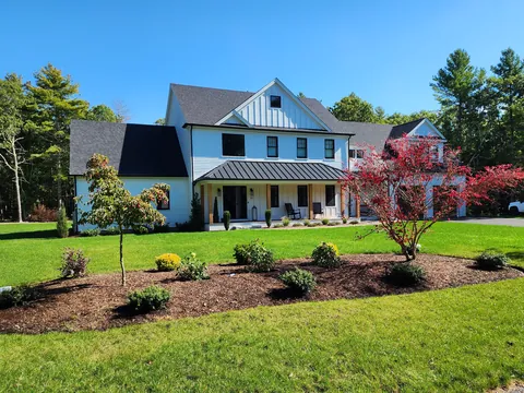 After: April 24, 2022: house wrap and windows in. October 2023: the same farmhouse finished, with its porch, siding and landscaping.