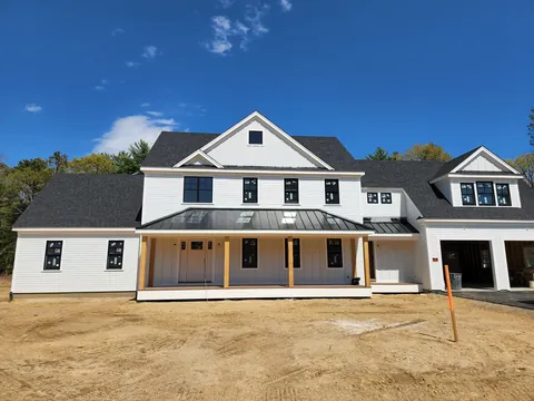 Large white farmhouse with a metal porch roof, nearly finished